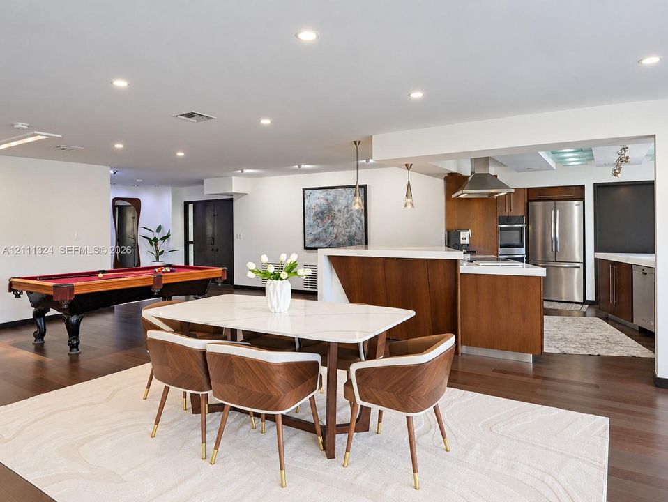 Open-concept interior featuring wood-finish flooring, recessed lighting, and a kitchen equipped with flat-panel wood cabinetry, stone countertops, and stainless steel appliances