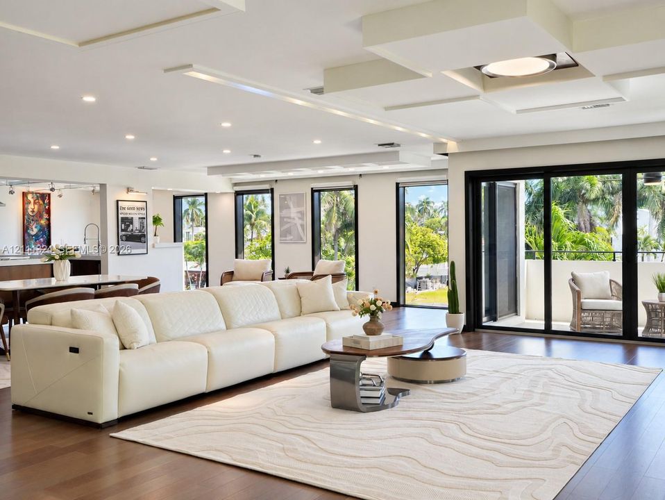 Open-concept living space featuring wood-finish flooring, custom tray ceiling with recessed lighting, and expansive floor-to-ceiling sliding glass doors