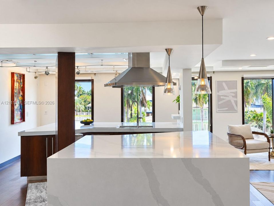 Kitchen featuring a waterfall-edge stone island, wood-finish cabinetry, stainless steel range hood, gooseneck faucet, and conical pendant lighting