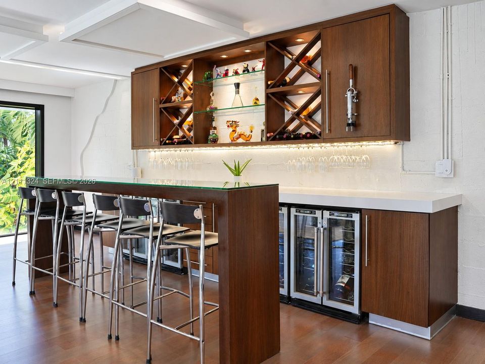Custom wet bar featuring wood-finish cabinetry, built-in wine storage, integrated under-cabinet lighting, and a glass-topped counter