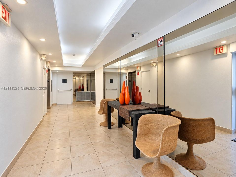 LOBBY-Hallway featuring tile flooring, recessed ceiling lighting, a tray ceiling detail, and floor-to-ceiling wall mirrors