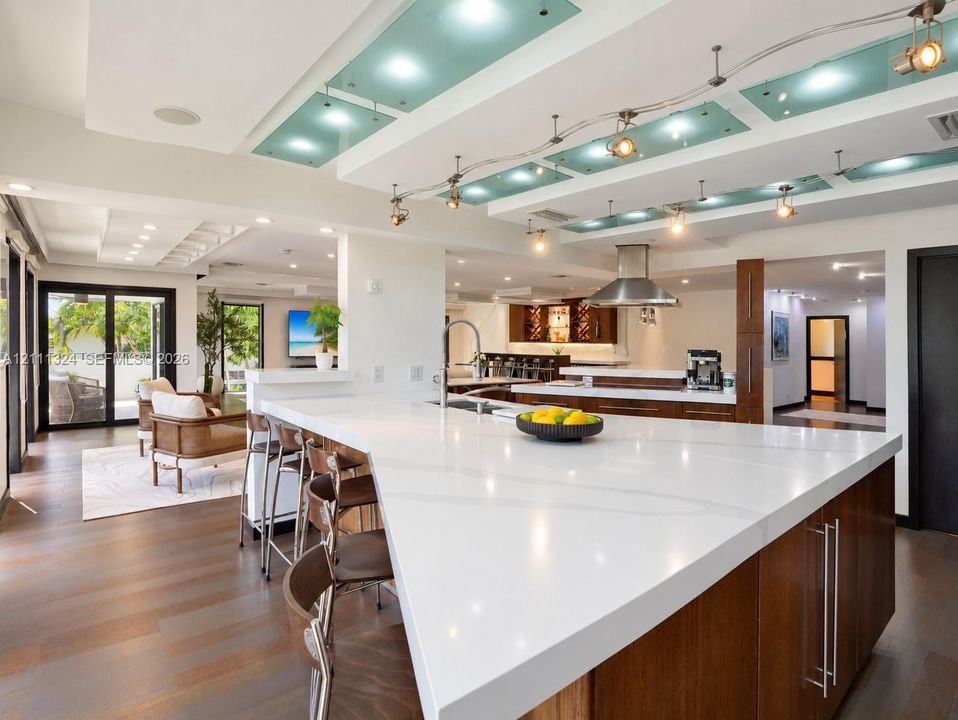 Kitchen featuring an oversized island with a solid surface countertop, wood-finish cabinetry, stainless steel range hood, recessed ceiling lighting with frosted glass panels, and wood-finish flooring