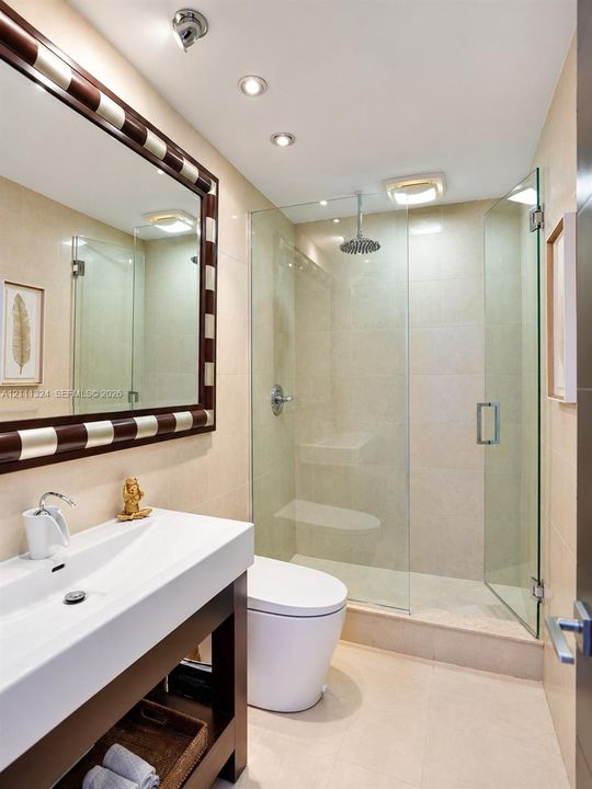 Bathroom featuring a floating vanity with a rectangular sink, walk-in shower with a glass enclosure and rain-style showerhead, recessed lighting, and large-format tile wall cladding