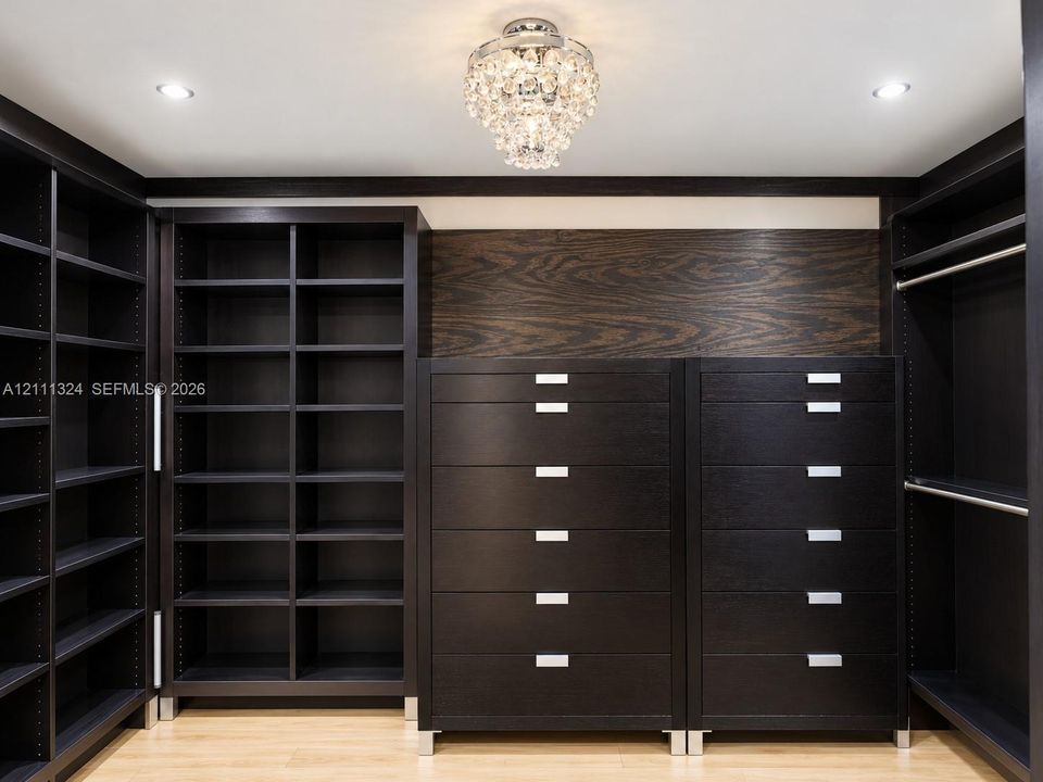 Custom wood-finish built-in cabinetry featuring extensive shelving, integrated drawer units with metallic hardware, and a center decorative crystal chandelier