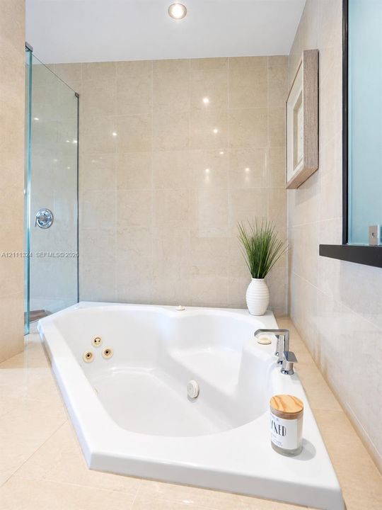 Jetted soaking tub with deck-mounted chrome faucet, recessed ceiling lighting, glass-enclosed shower, and floor-to-ceiling tile surround