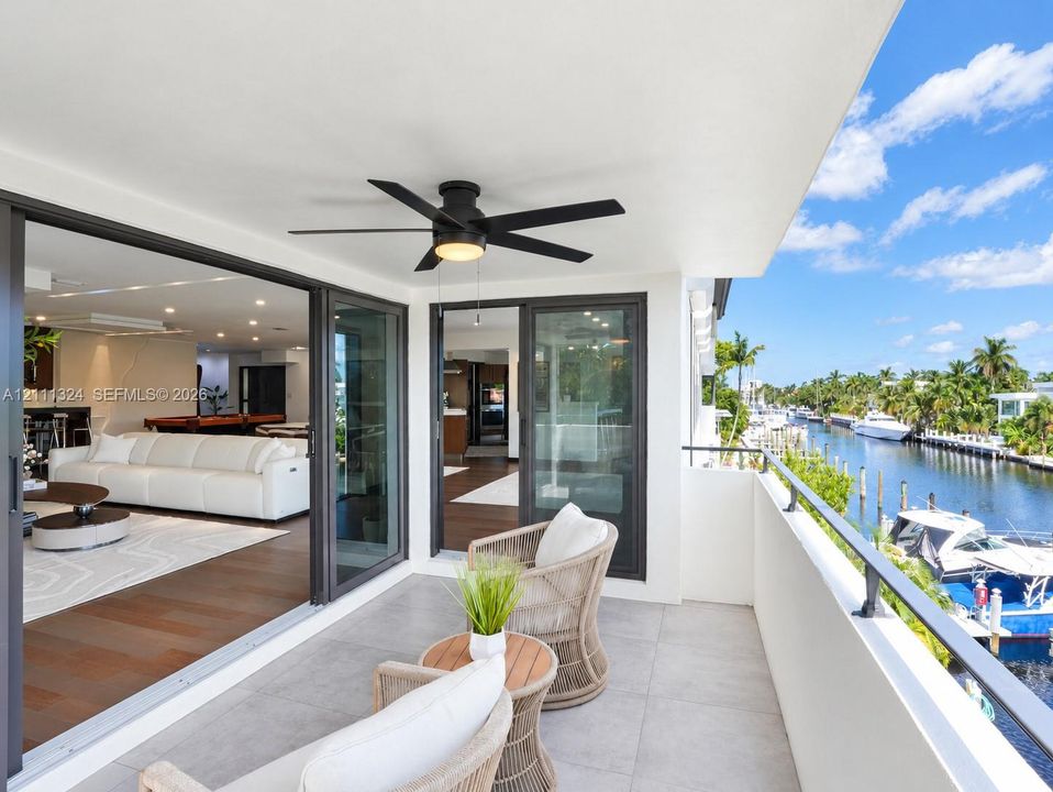 Covered balcony featuring oversized neutral floor tiles, a matte black ceiling fan with integrated lighting, and dark-framed sliding glass doors