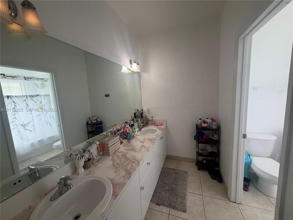 Full-width vanity featuring dual oval drop-in sinks, stone-patterned countertop, white cabinetry, expansive wall-mounted mirror, and tile flooring