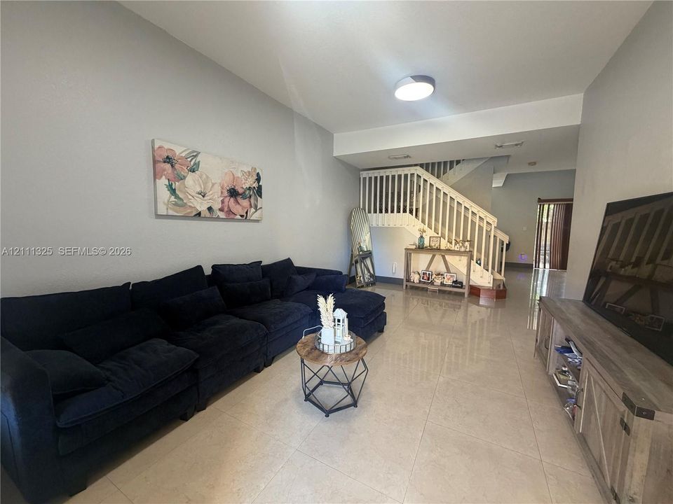 Open-concept interior featuring large-format tile flooring, a painted wooden staircase with balustrades, and a recessed ceiling lighting fixture