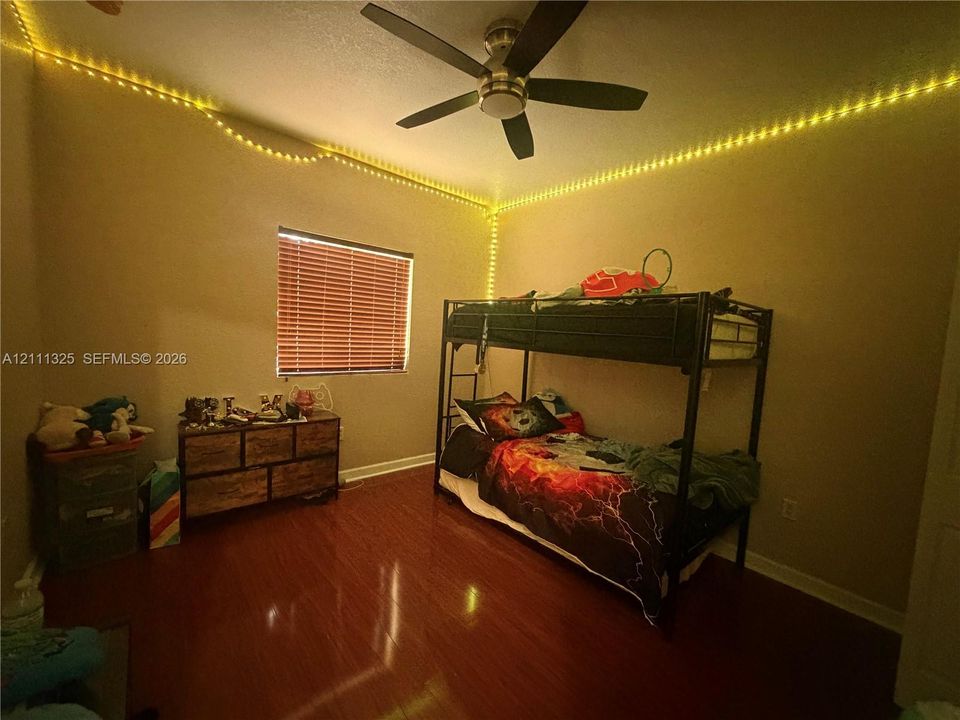 Interior room featuring wood-finish flooring, a ceiling fan with integrated lighting, and a window with horizontal blinds