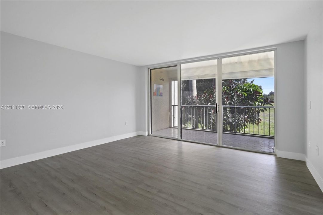 Living area featuring wood-look laminate flooring, crisp white  walls, and expansive floor-to-ceiling sliding glass doors opening to a private screened-in balcony.
