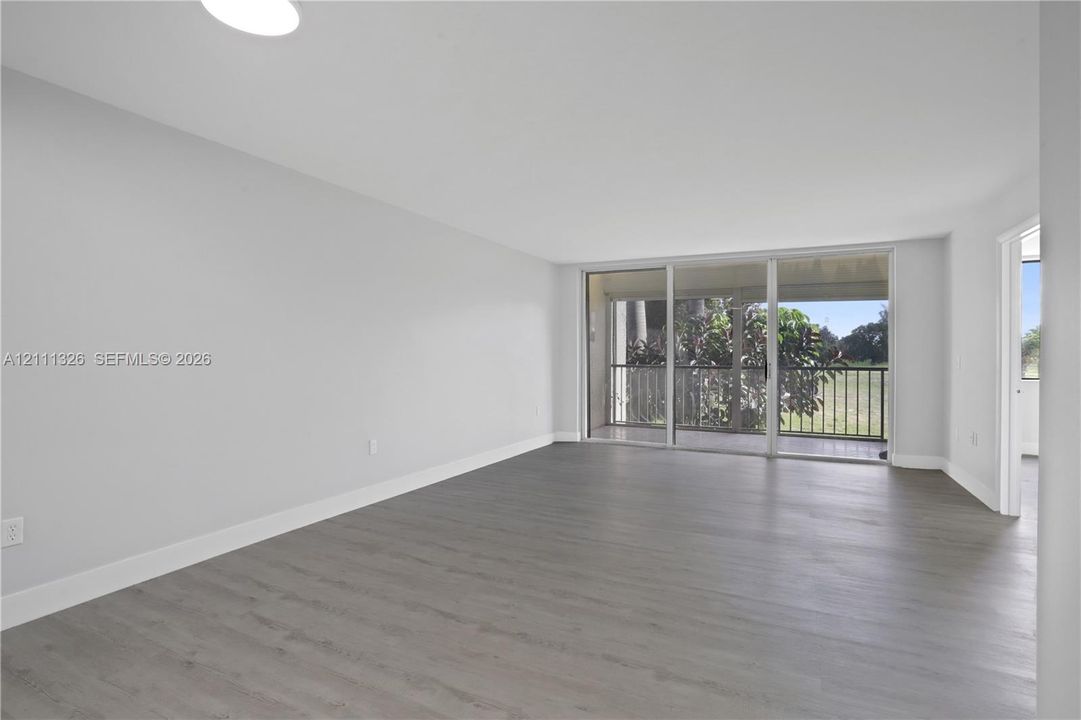 Open-concept interior featuring neutral walls, wood-finish flooring, and sliding glass doors leading to a covered screened-in balcony.