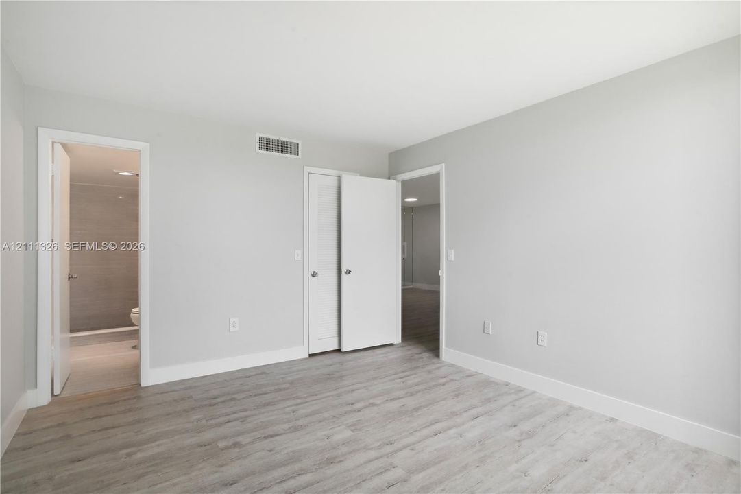 Primary bedroom featuring crisp white walls, laminate wood-look flooring, and a walk-in closet and en suite bathroom with a walk-in shower.