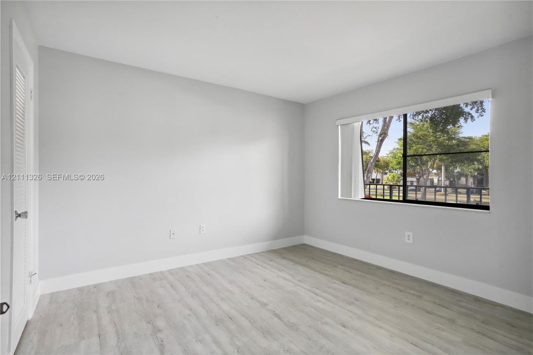 Second bedroom with neutral-toned interior featuring wood-look laminate flooring, a large window with black frames, and a walk-in closet.