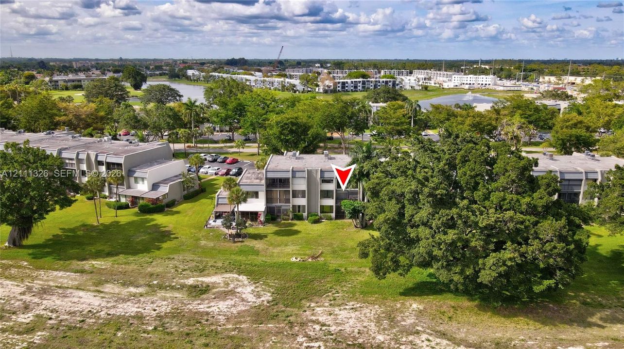 Aerial exterior view from the back of the unit looking North featuring balconies, concrete exterior siding, and expansive surrounding green space with mature landscaping.