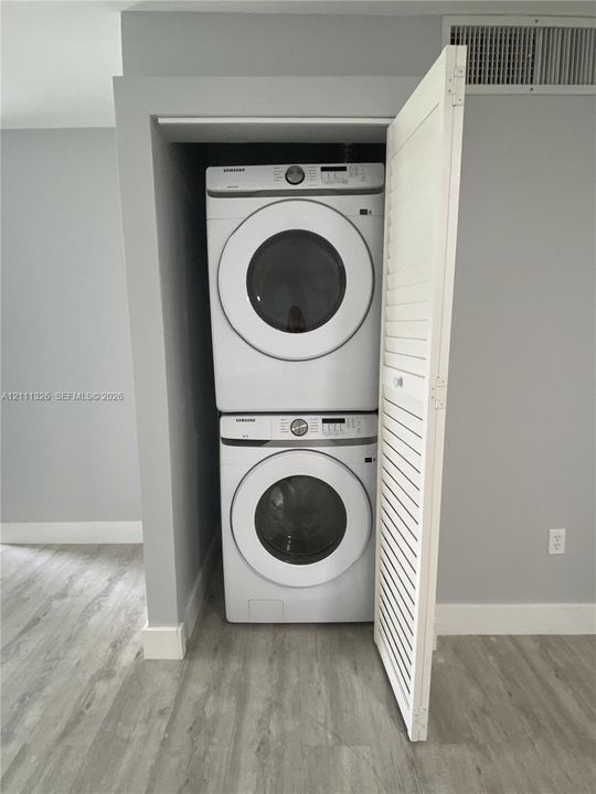 Dedicated laundry alcove featuring stacked, full sized high-capacity front-load washer and dryer units enclosed by a white louvered door