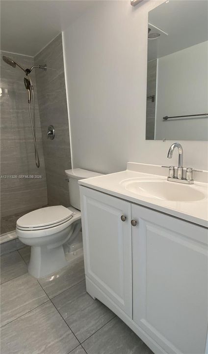Bathroom featuring a white vanity cabinet with a solid surface countertop, an integrated sink basin, a walk-in shower with horizontal-patterned wall tile, and large-format floor tile