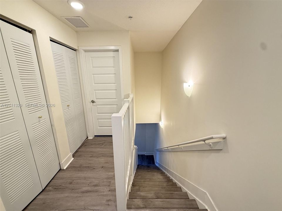 Hallway featuring wood-finish flooring, two sets of louvered bifold closet doors, a multi-panel interior door, and wall-mounted sconce lighting
