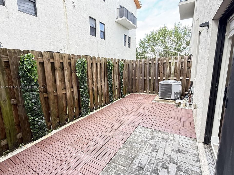 Private patio area featuring modular composite decking, gray stone paver accents, and a full-perimeter wood privacy fence