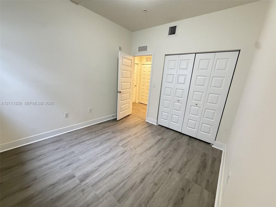 Room featuring wood-finish flooring, high ceilings, white panel interior doors, and a double-door closet with square-panel detailing