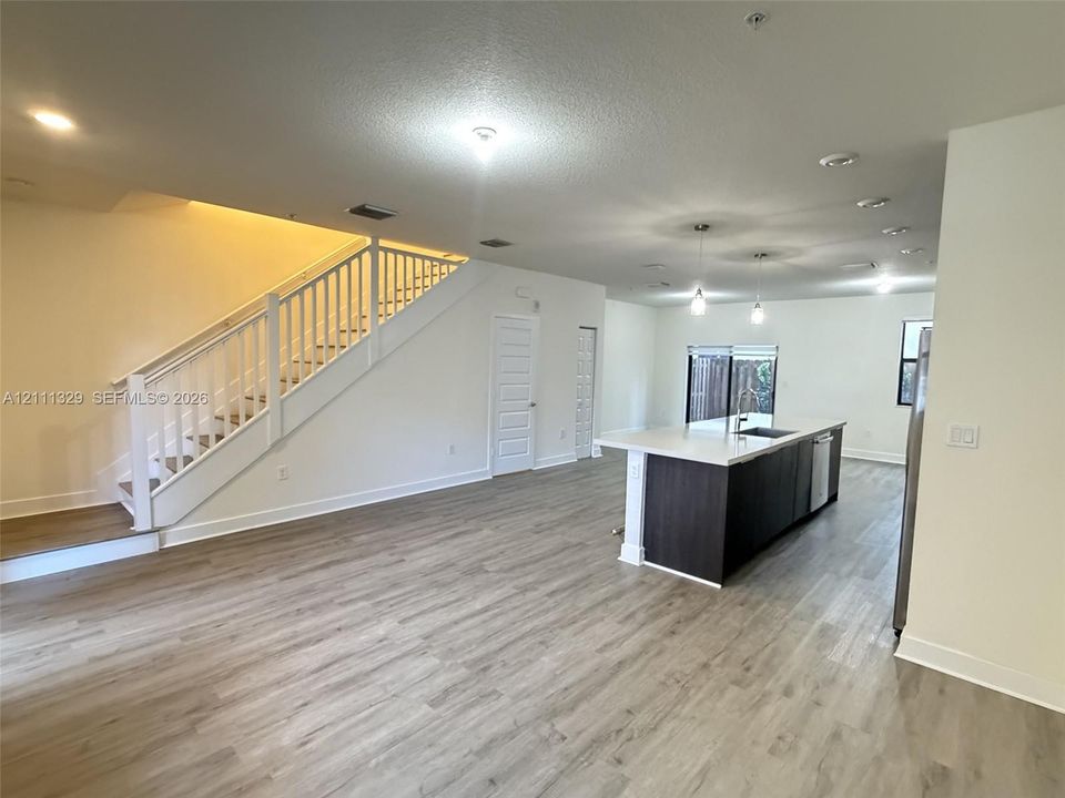 Open-concept interior featuring wood-finish flooring, a kitchen island with quartz countertops, custom cabinetry, pendant lighting, and a staircase with white balusters