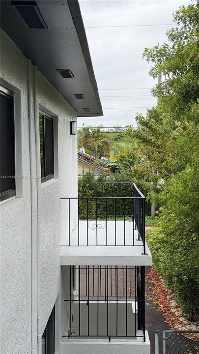 Stucco exterior featuring dual-level outdoor balconies with black metal railings, recessed soffit lighting, and window screens