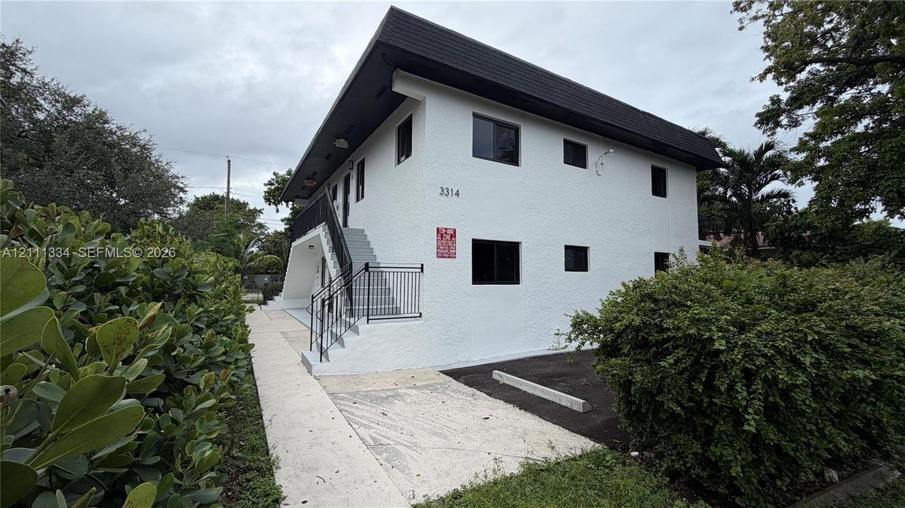 Two-story exterior featuring white stucco siding, a flat roofline, black metal handrails, and surface-level parking