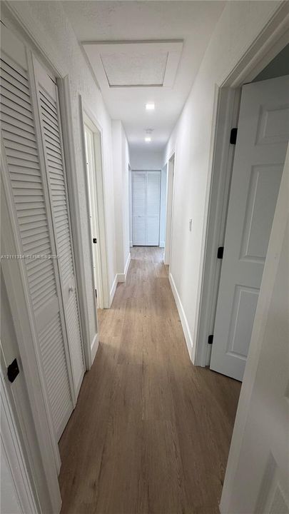 Hallway featuring wood-finish flooring, white paneled doors, louvered closet doors, and recessed lighting