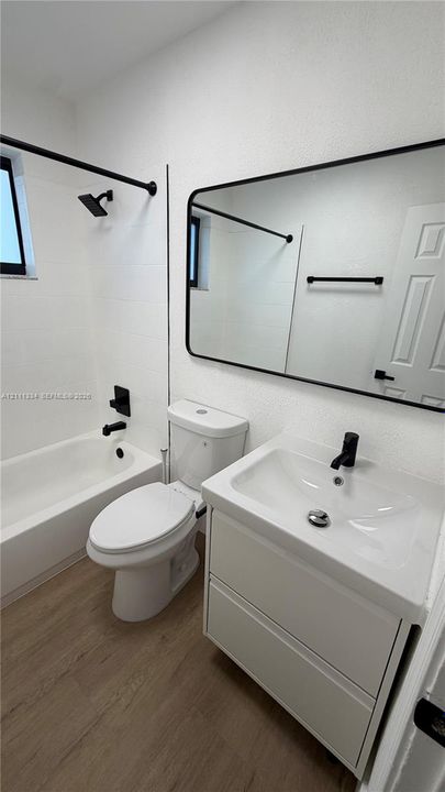 Bathroom featuring a vanity with integrated sink, black matte hardware, framed mirror, and wood-finish flooring