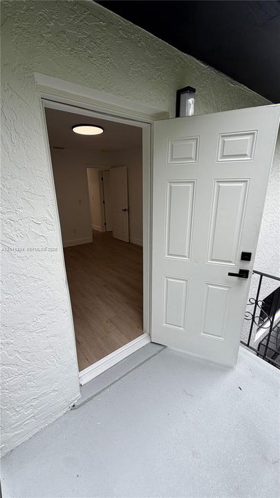 Six-panel entry door featuring a matte black electronic deadbolt and handle set, textured exterior wall finish, wood-finish flooring, and recessed circular ceiling lighting
