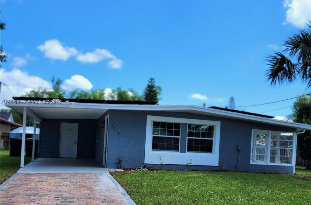 Single-story residence featuring a paved brick driveway, attached carport, solar panel system, and multi-pane windows with white trim