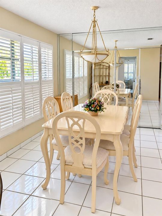 Dining space featuring white ceramic tile flooring, full-wall mirrored panels, plantation shutters, and a multi-arm metal chandelier