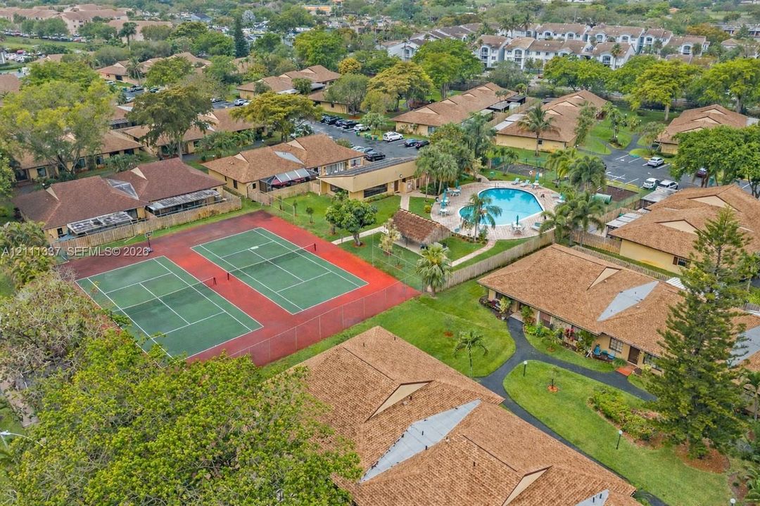 Aerial perspective of a residential community featuring dual outdoor tennis courts, a swimming pool, pedestrian walkways, and mature landscaping