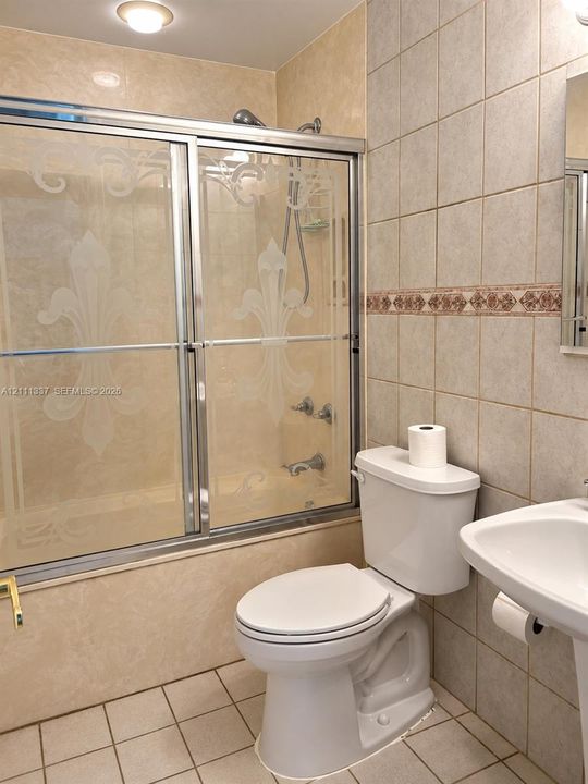 Shower enclosure with decorative etched glass doors, ceramic wall tiling featuring a detailed border accent, and a pedestal sink