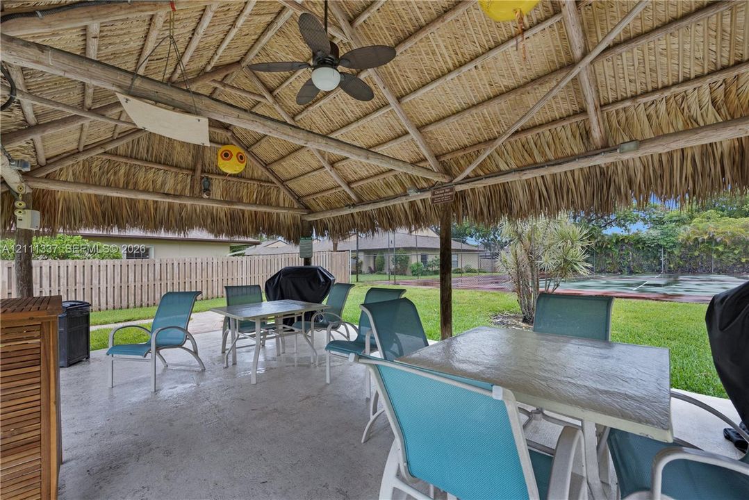 Outdoor tiki-style thatched roof pavilion featuring a concrete patio, exposed wooden support beams, and an integrated ceiling fan