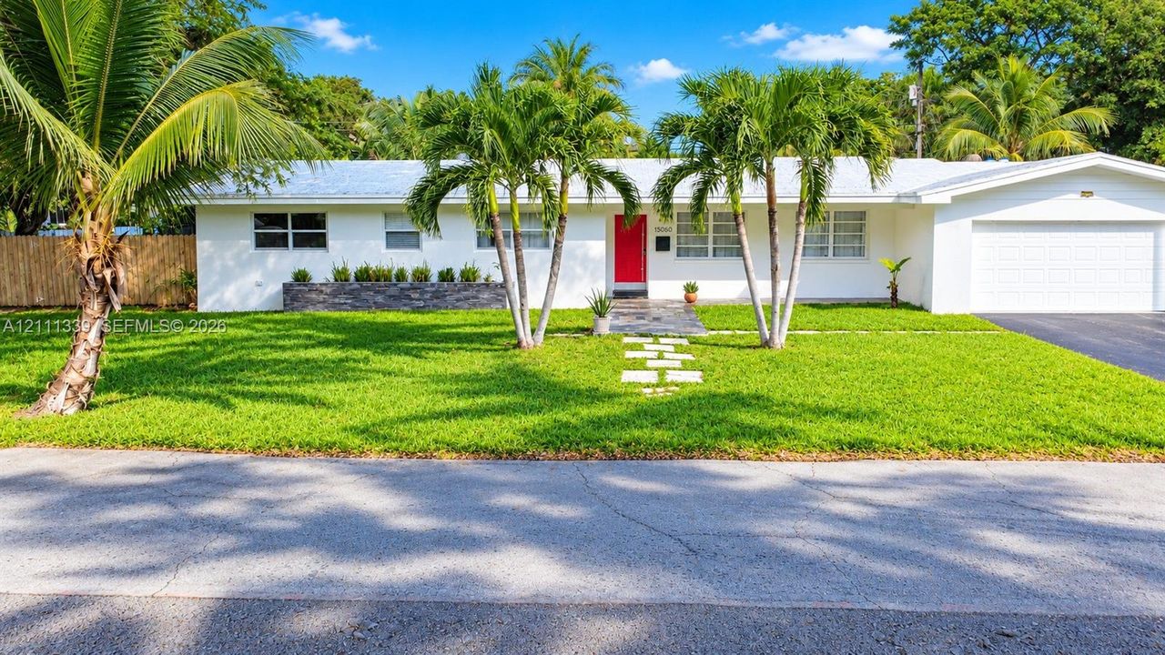 Single-story exterior featuring white stucco siding, a stone-accented planter box, a vibrant red entry door, a stone paver walkway, and an attached two-car garage