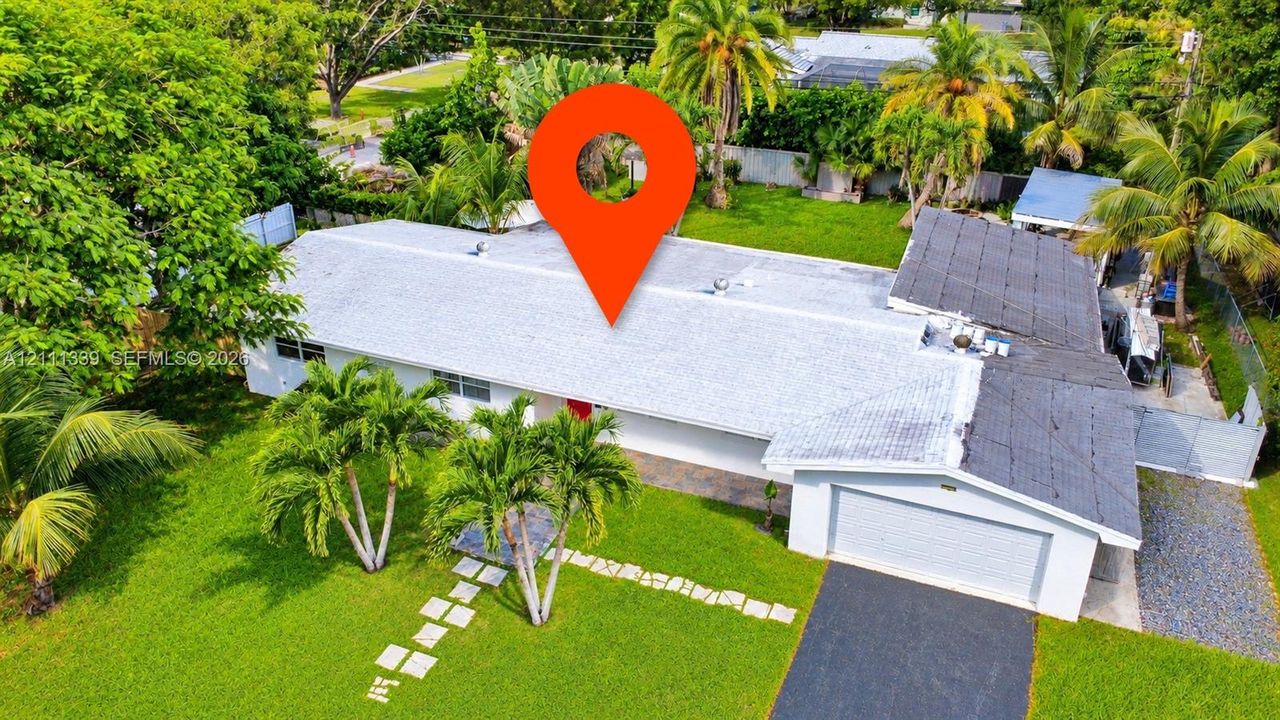 Single-story residence featuring an asphalt driveway, an attached garage, and stone paver walkway, situated on a lot with mature palm trees and established landscaping