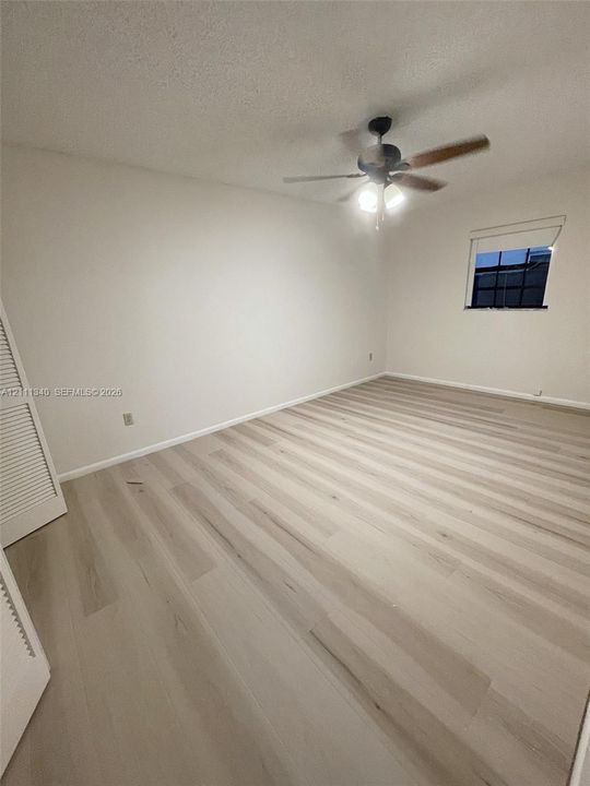 Room featuring wood-finish flooring, a ceiling fan with integrated lighting, and a closet with louvered doors