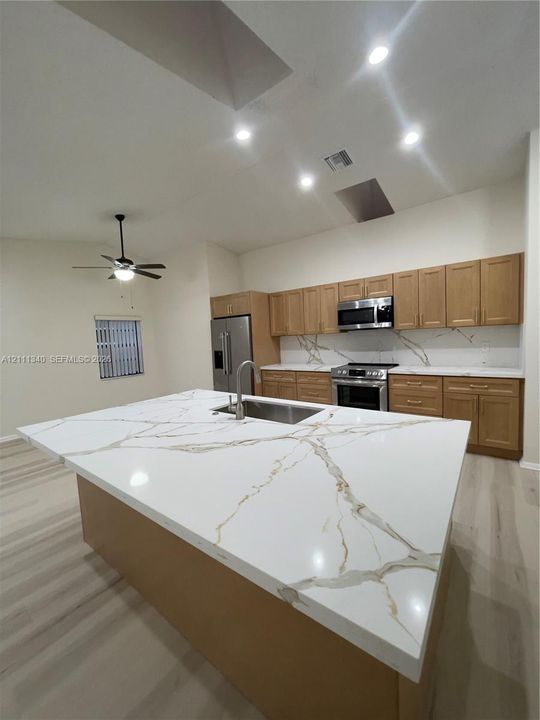Kitchen featuring a large central island with veined stone-patterned countertops, wood-finish cabinetry, stainless steel appliances, recessed ceiling lighting, and wood-finish flooring