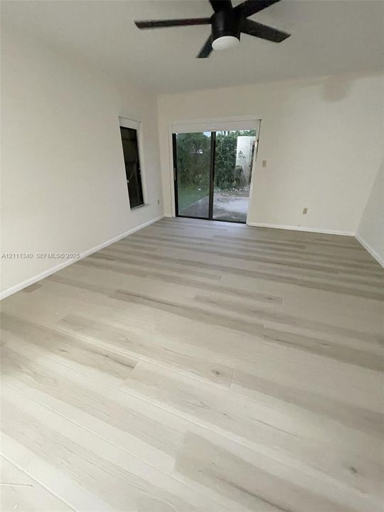 Room featuring wood-finish flooring, a matte black ceiling fan, and sliding glass doors