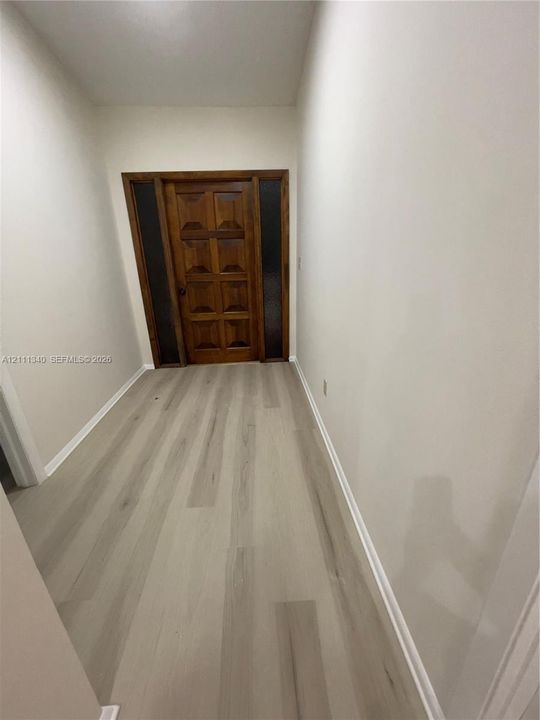 Solid wood-finish front door with symmetrical glass side panels and neutral-toned wood-finish flooring