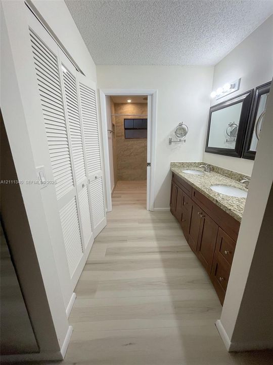 Dual-sink vanity with stone-finish countertop, wood-finish cabinetry, louvered-style closet doors, and wood-finish flooring