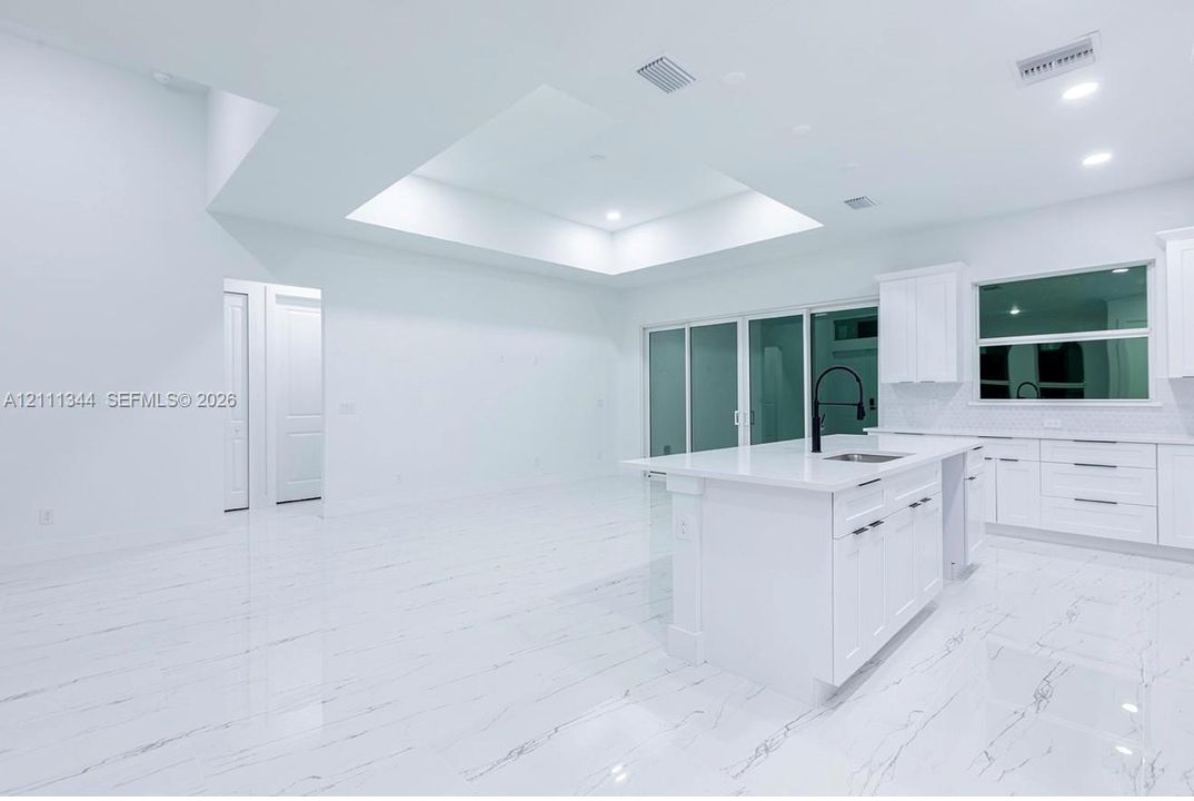 Kitchen featuring a central island with a quartz countertop, stone-finish tile flooring, recessed tray ceiling, white cabinetry with matte black hardware, and floor-to-ceiling glass sliding doors