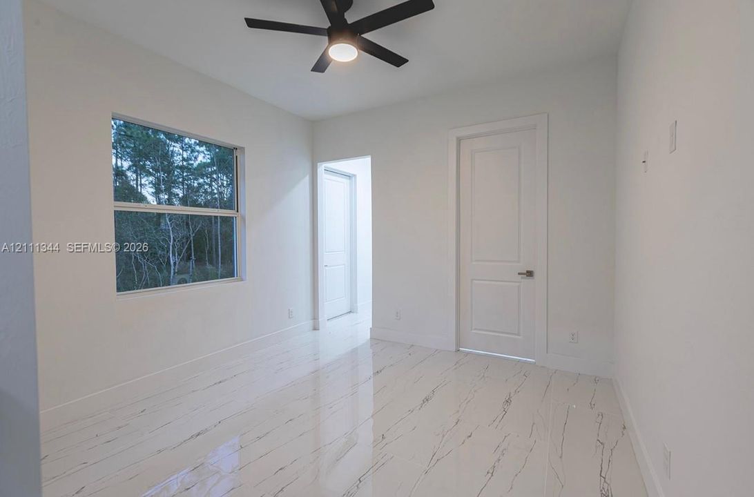Neutral interior featuring polished stone-finish flooring, a matte black ceiling fan, and a single-hung window with exterior greenery