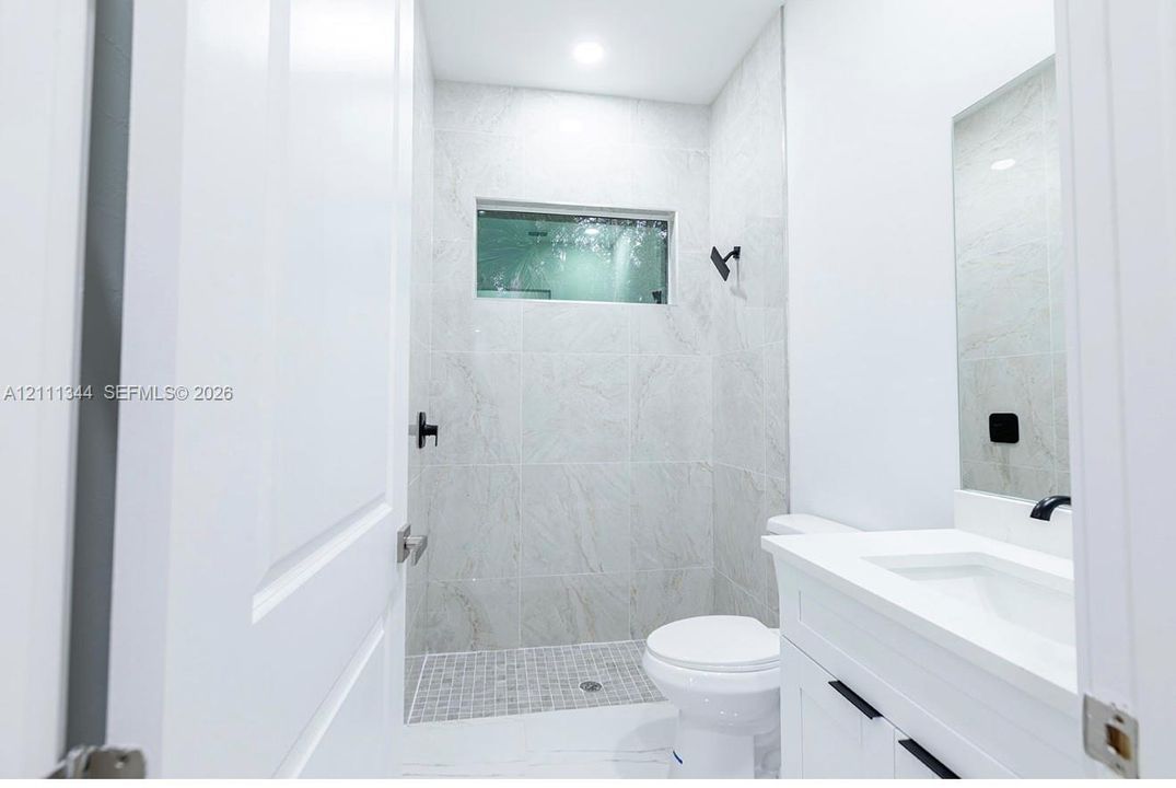 Bathroom featuring a shower stall with full-height tile surrounds, a transom window, matte black hardware, and a white vanity with an integrated sink