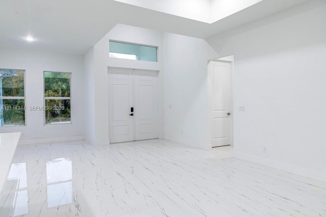 Double-door entry featuring a transom window, high ceilings, large-format tile flooring with veining detail, and tall, multi-pane windows