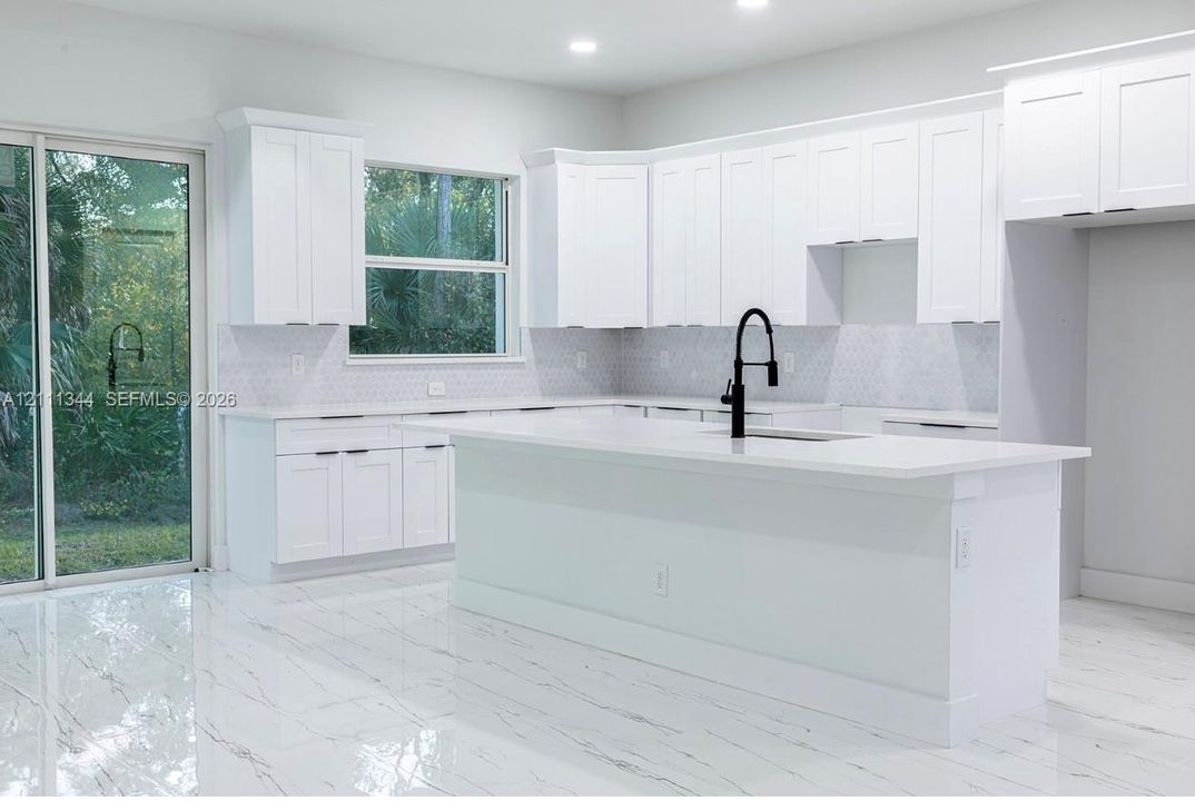 Kitchen featuring white Shaker-style cabinetry, a central island with a quartz countertop, geometric pattern backsplash, polished stone-finish flooring, and a matte black gooseneck faucet