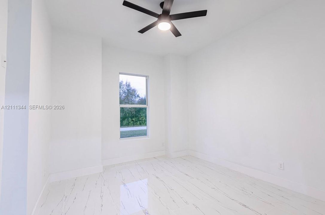 Room featuring white stone-finish tile flooring, a dual-pane window, and a matte black ceiling fan with integrated lighting