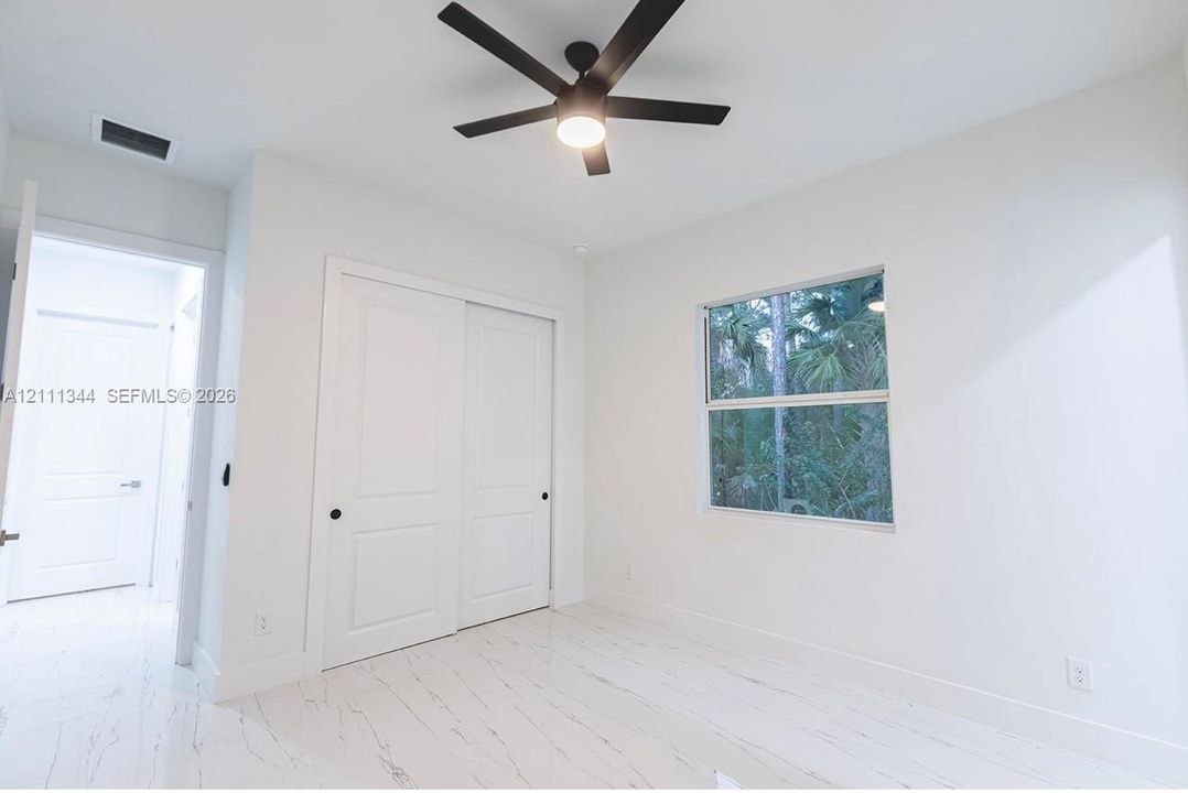 Neutral-toned room featuring light-colored flooring with marble-finish detailing, a ceiling fan with integrated lighting, and a dual-panel sliding closet door