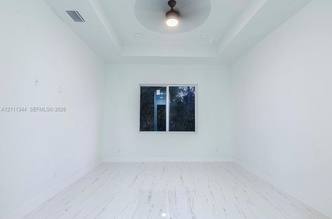 Tray ceiling featuring a central matte black ceiling fan, stone-patterned tile flooring, and a single-pane window