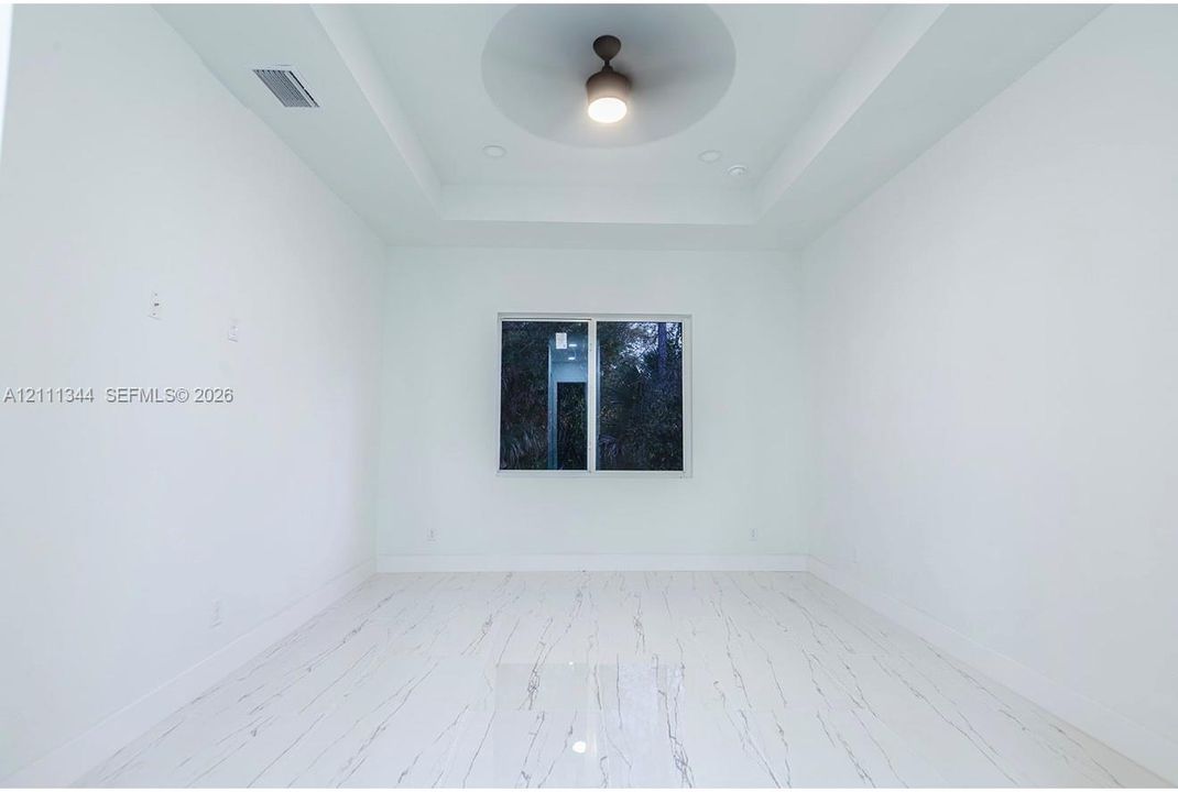 Interior room featuring a tray ceiling with a central integrated lighting fixture, white stone-patterned flooring, and a sliding window
